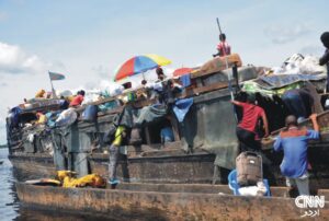 Rescue teams searching the Congo River after a deadly boat capsizing incident; smoke and debris visible in the background.